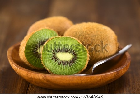 Kiwifruits on wooden plate with spoon (Selective Focus, Focus on the half kiwi)