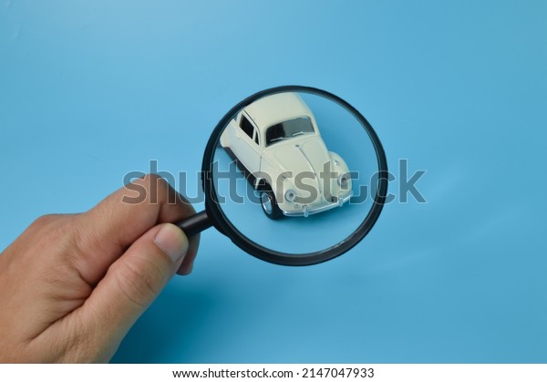 Klang, Malaysia:\
April 18, 2022- White retro car model and magnifying glass. Find a\
car and car search\
concept