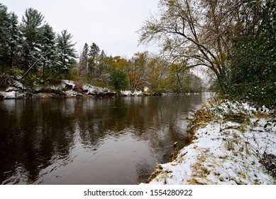 Kletzsch Park Where The Milwaukee River Passes Through With Snow On The Riverbanks And In The Fall Foilage For Overlapping Winter And Autumn In Early November. 