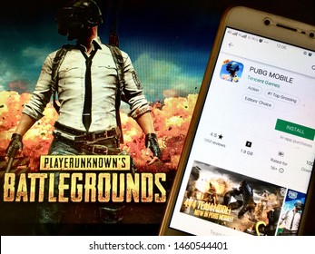 Kluang, Johor / Malaysia - July 25, 2019 : A man holding the PUBG Mobile app in front PUBG wallpaper. PUBG also known as PlayerUnknown’s Battlegrounds is an online multiplayer battle royale game.