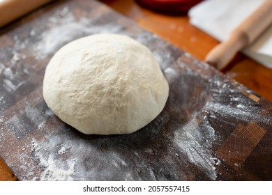 Kneaded Yeast Dough Formed Into A Large Bowl. Against The Background Of A Wooden Board With Dusty Flour. Baking Technique In The Home Kitchen.