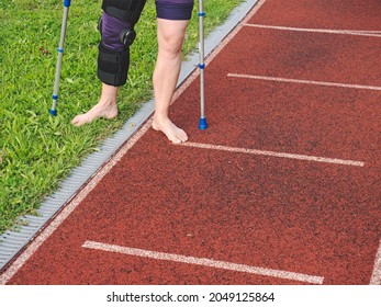 Knee With Knee Brace Support After Surgery With Walking Stick On Red Stadium Racetrack