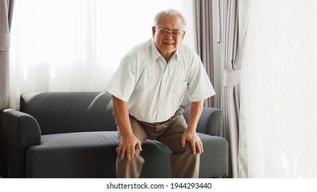 Knee Problem Of Senior, Has Leg Pain When Standing Up And Sitting Down During Old Age. Asian Senior Has Knee Pain After Stand Up And Sit Down In Living Room At Home.