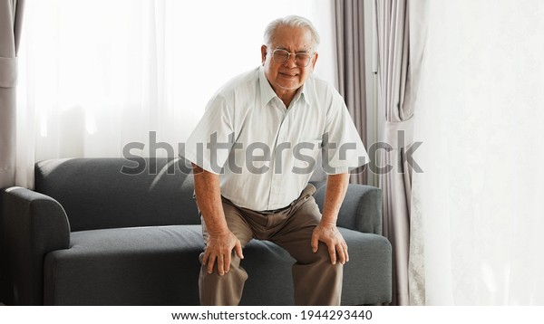 Knee problem of senior, has\
leg pain when standing up and sitting down during old age. Asian\
senior has knee pain after stand up and sit down in living room at\
home.