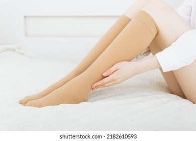 Knee Socks Or Socks. Beige Compression Stockings On A Woman In A White Room. Girl Putting On Stockings At Home. Beautiful Female Legs.