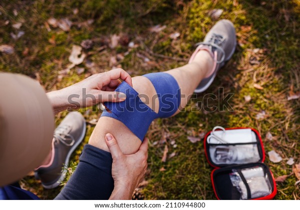 Knee sprain fixation during hiking.\
Injured woman using elastic bandage from first aid\
kit