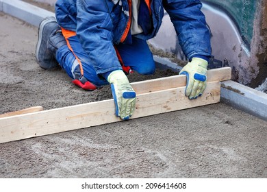 A kneeling blue overalls laborer levels a sandy foundation with a wooden level for future sidewalk cladding. Copy space.