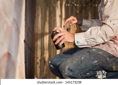 Kneeling Graffiti Artist Spray Painting A Wall