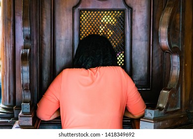 kneeling woman at the confessional confesses with the priest