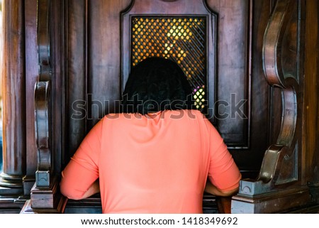 kneeling woman at the confessional confesses with the priest