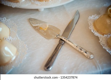 Knife And A Cake Cutter On A Wedding Table. Silver Cake Servers For Cookies On White Tablecloth. Close-up