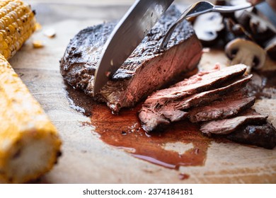 knife cutting juicy medium rare grilled steak on wooden board  - Shutterstock ID 2374184181
