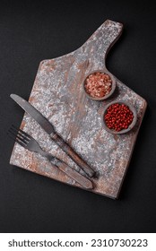 Knife, fork and cutting board, salt, pepper and other ingredients located on a textured concrete background - Shutterstock ID 2310730223