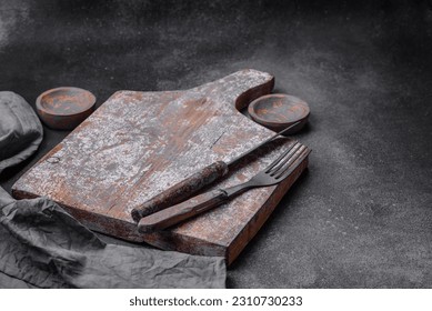 Knife, fork and cutting board, salt, pepper and other ingredients located on a textured concrete background - Shutterstock ID 2310730233