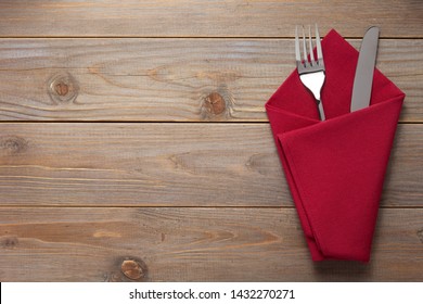 Knife And Fork In Napkin At Rustic Wooden Plank Board Table Background, Top View