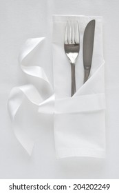 Knife and fork table setting with white linen and satin ribbon