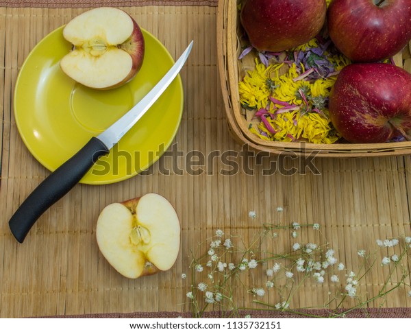 Knife and half of apple are on
yellow dish at bamboo tablecloth with basket and second
part