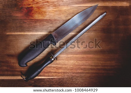 a knife and a kinfe sharpner kitchen tool close up over a rustic wooden background