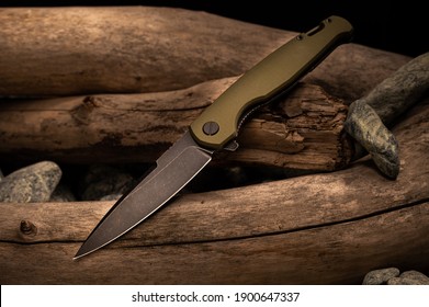 Knife with olive handle and black blade. Knife lying on wood. Front view.