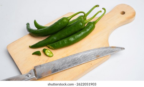 Un cuchillo está en una tabla de cortar con un montón de pimientos verdes. El cuchillo está apagado y los pimientos se cortan por la mitad