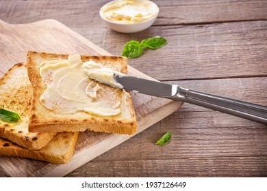 Messer, das Butter auf Toastbrot auf Holzhintergrund ausbreitet.