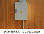 Knife switch and high voltage hazard sign on the wooden wall of house. Yellow electrical warning danger triangle symbol and metal security fence box. Closed lock electric panel transformer substation
