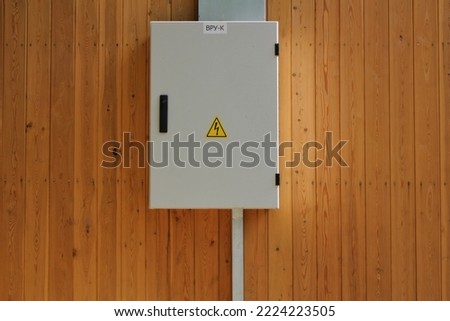 Knife switch and high voltage hazard sign on the wooden wall of house. Yellow electrical warning danger triangle symbol and metal security fence box. Closed lock electric panel transformer substation
