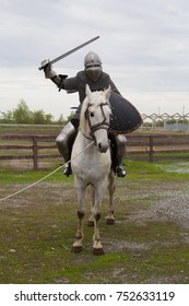 A knight is riding a white horse with a sword in his hand. A man in armor. A model in chain mail. Medieval armor