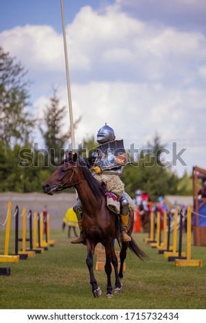 A knight in vintage armor of the 15th century rides a horse across a field for a tournament