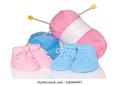 Knitted baby booties with blue and pink wool plus knitting needles, isolated on a white background. - Powered by Shutterstock