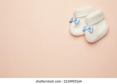 Knitted baby booties on light pink background, flat lay. space for text