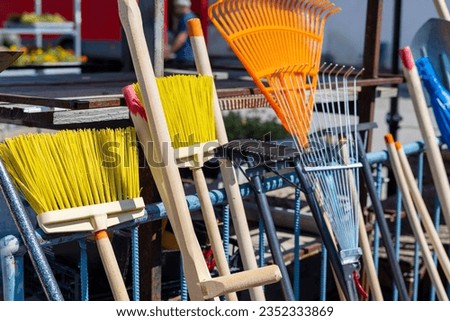 knitted brooms made from plants, outdoor street with plastic rope threads, garden rake with wooden handle.market, products for sale, store shop sunny summer day