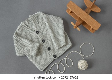 knitted children's cardigan with a ball of natural yarn on a gray background with a wooden toy in retro style, baby  layout