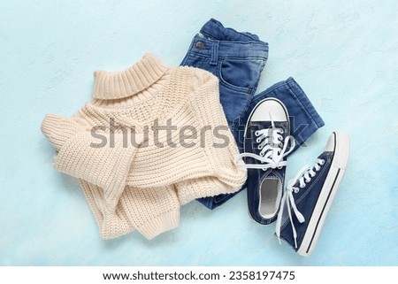 Knitted children's sweater, jeans and gumshoes on color background