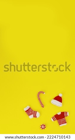 knitted Christmas handmade decorations ornaments sock, sweater, hat and caramel in red and whitecolors on yellow background, banner, copy space, vertical, 16:9