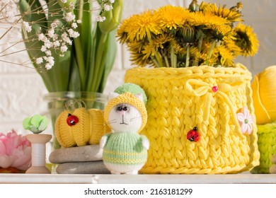 a knitted green-yellow kitten sits with knitting needles under flowers, A blooming bouquet of tulips. Creative workshop on handmade needlework