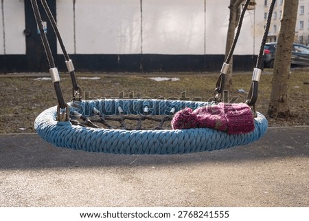Knitted hat left on an empty rope swing in a playground during mild spring weather, illustrating a seasonal transition and the common occurrence of misplaced personal items
