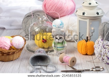 a knitted kitten with knitting needles and orange pumpkins, colored balls of thread in a basket. Creative workshop on handmade needlework