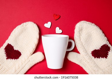 Knitted mittens, cup and paper hearts on red background, flat lay