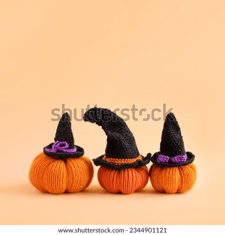 Knitted orange pumpkins with a black witch hat on an orange background, autumn composition, front view. Halloween concept.