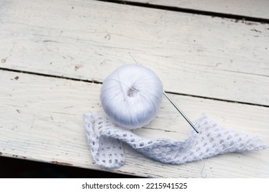 Knitted Pattern Next To A Spool Of Thread And A Crochet Lies On The Edge Of A Wooden Table. Copy Space. View From Above