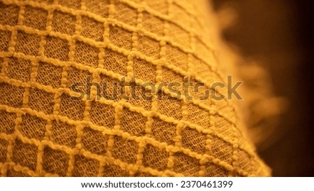 Knitted plaid with geometric pattern as background. Orange handmade warm woven blanket with wrinkles and rhombuses ornament. Soft knitwear accessory for cold weather season comfort