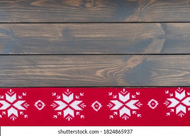 knitted red blanket with traditional christmas pattern at the bottom on dark wooden background. Copy space for text.