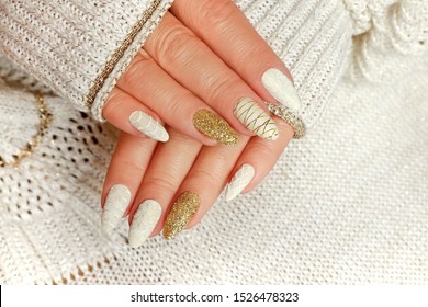 Knitted sand manicure on long oval nails with golden sequins and threads on the female red in a jacket. Winter trend in nail design.