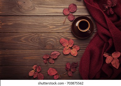 Knitted scarf of burgundy color with autumn leaves and a cup of coffee on a dark wooden background. Top view. Flat lay. Foto Stok