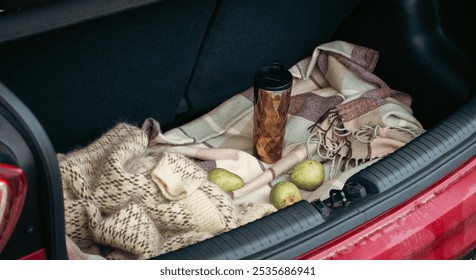 Knitted sweater, three pear fruits and thermos mug on checkered blanket in open car trunk. Autumn still life. Road trip picnic. Travel lifestyle moments. Fruits and coffee mug in trunk car. - Powered by Shutterstock