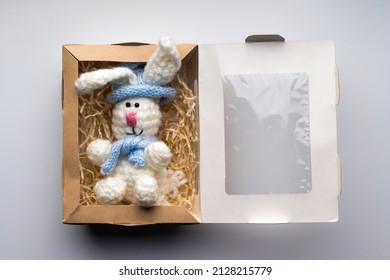 Knitted toy bunny in a cardboard box with paper filler. Handmade gift