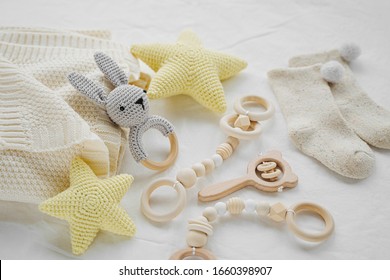 Knitted Toy Bunny, Yellow Stars And Wooden Teether For Newborn On White Bed. Gender Neutral  Baby Stuff And Accessories.