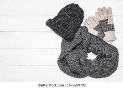 Knitted warm hat, scarf and gloves on a white wooden background. Winter clothes. Accessories. Flat lay. Top view. Fashion. Space. Grey colour