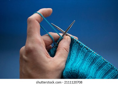 knitting needles in the hands of a knitter on a blue background close-up, knitted fabric